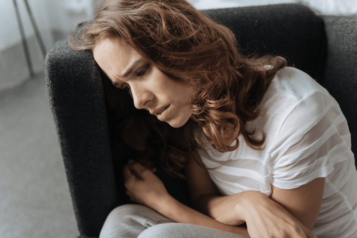 Woman leaning against a couch looking distressed, reflecting mood changes linked to bipolar disorder and hormones in women.
