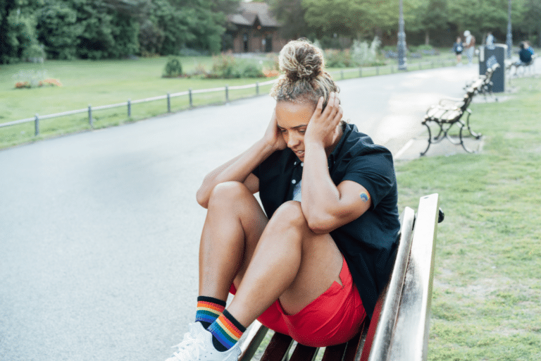 LGBTQ person sitting alone on a park bench, reflecting minority stress and emotional distress.