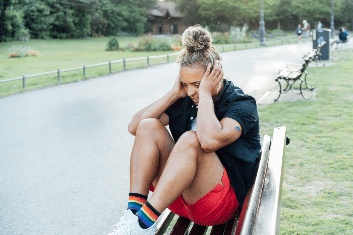 LGBTQ person sitting alone on a park bench, reflecting minority stress and emotional distress.