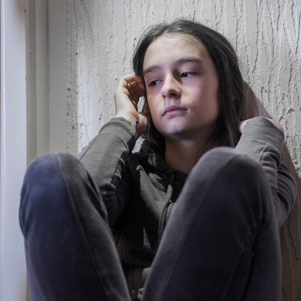 Teen girl sitting alone by a window, showing one of the teen depression signs parents may miss.