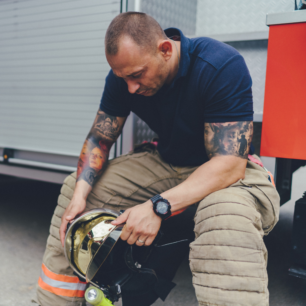 Firefighter sitting with his helmet after duty, reflecting the stress and career fears around seeking mental health help.