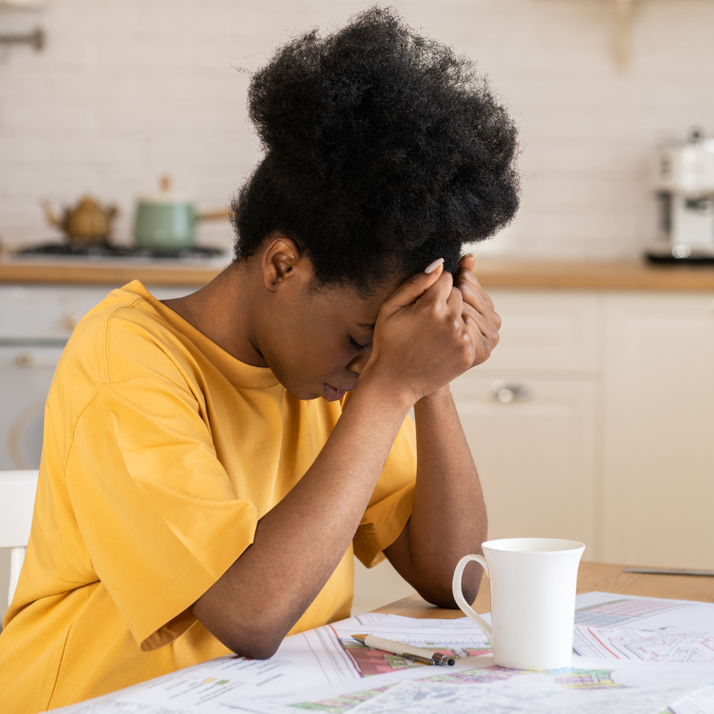 Parent sitting with head down at a table, showing the emotional toll of supporting a child with ADHD homework.