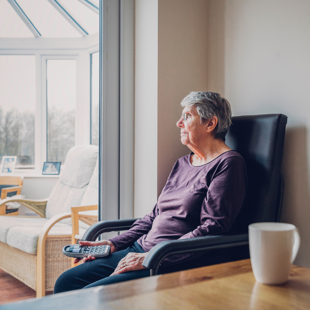 Older woman sitting alone by a window, reflecting social isolation and reduced daily connection after 65.