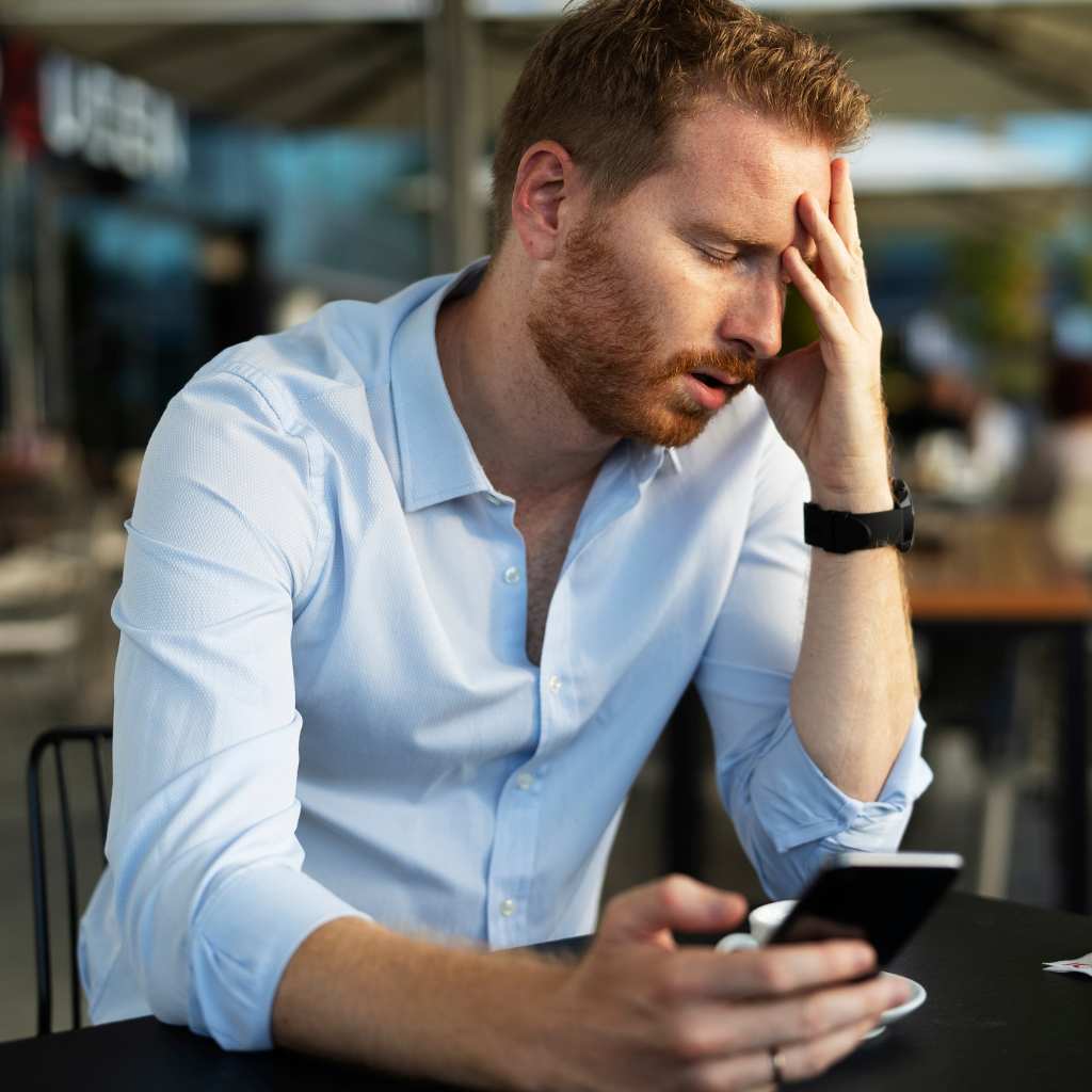 Man holding phone with hand on forehead, showing how health anxiety can intensify after searching symptoms.