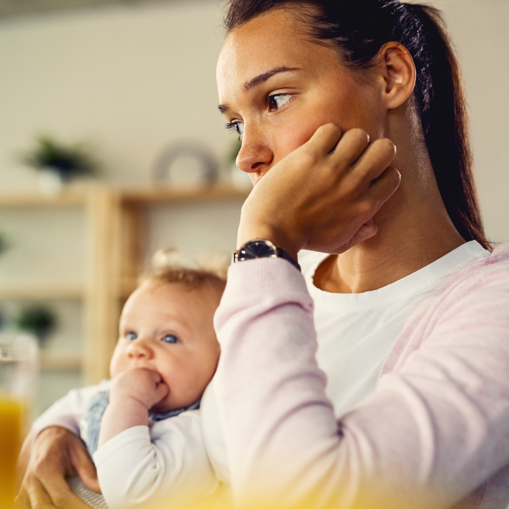 New mother holding her baby while looking worried, reflecting postpartum anxiety after birth.