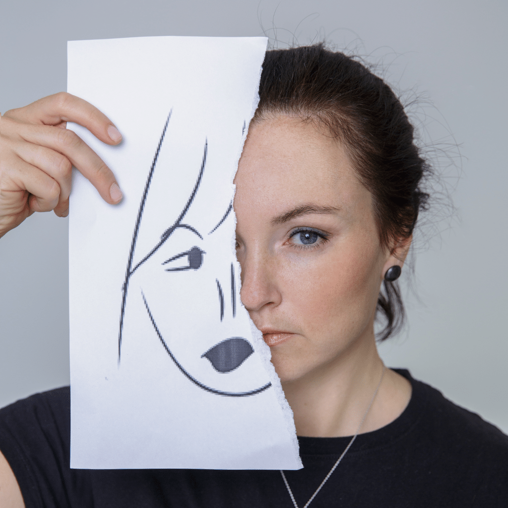 Woman holding a torn paper mask beside her face, reflecting mood changes linked to bipolar disorder and hormones.