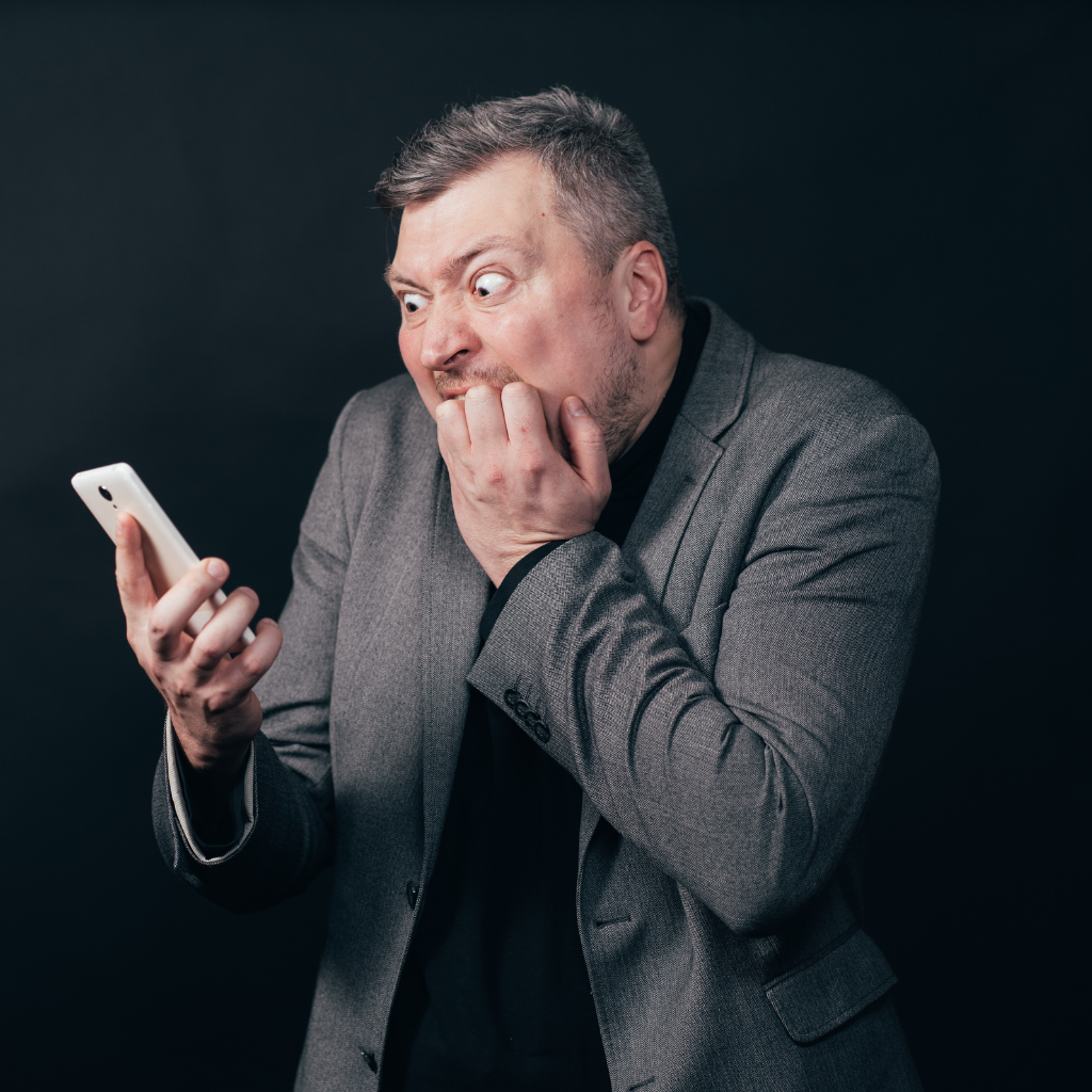 Man looking frightened while holding a phone, showing the fear and distress associated with phone anxiety.
