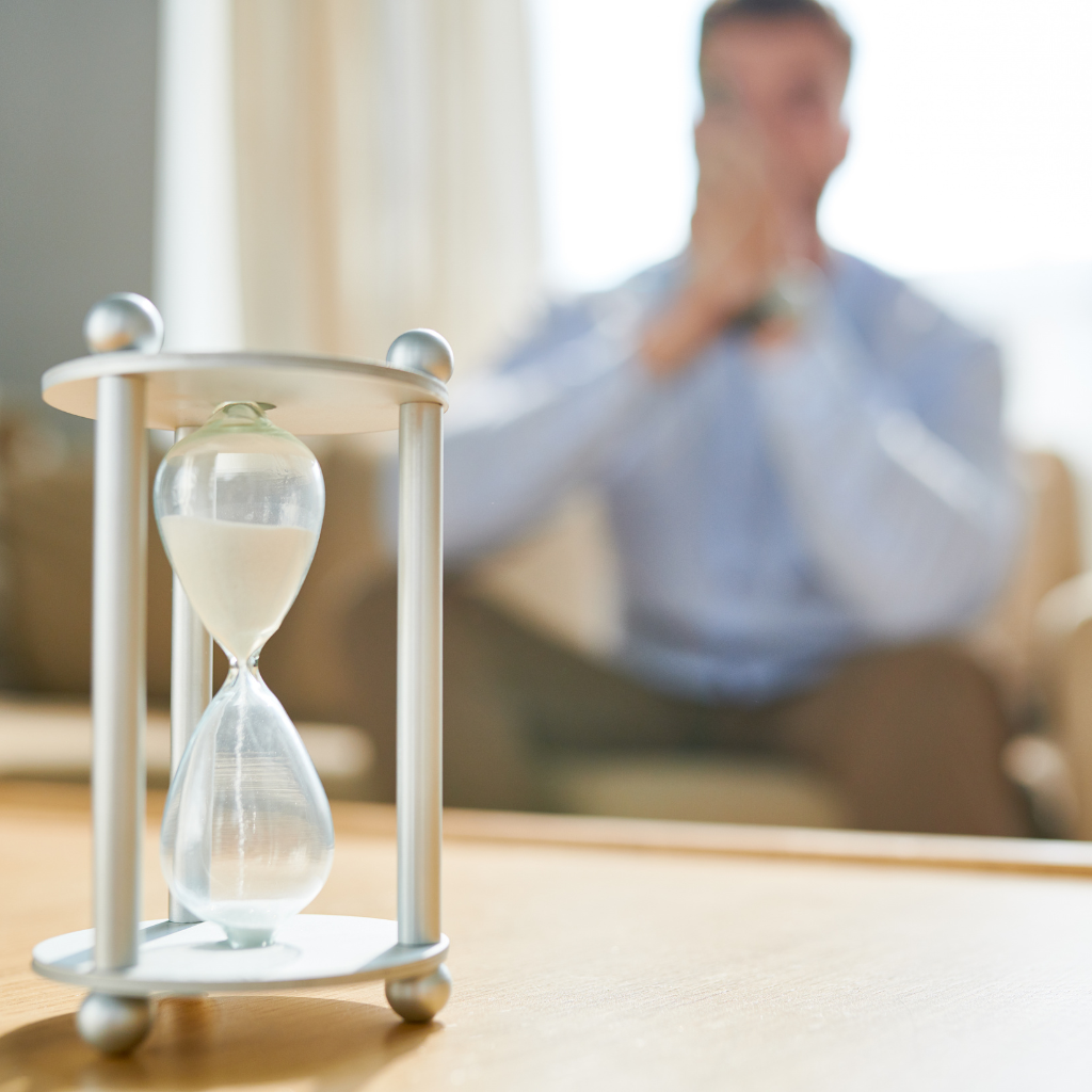 What to Do While You Wait for a Child Psychiatric Evaluation 1 Hourglass on a table with a worried parent blurred in the background, representing the wait for child psychiatric care.