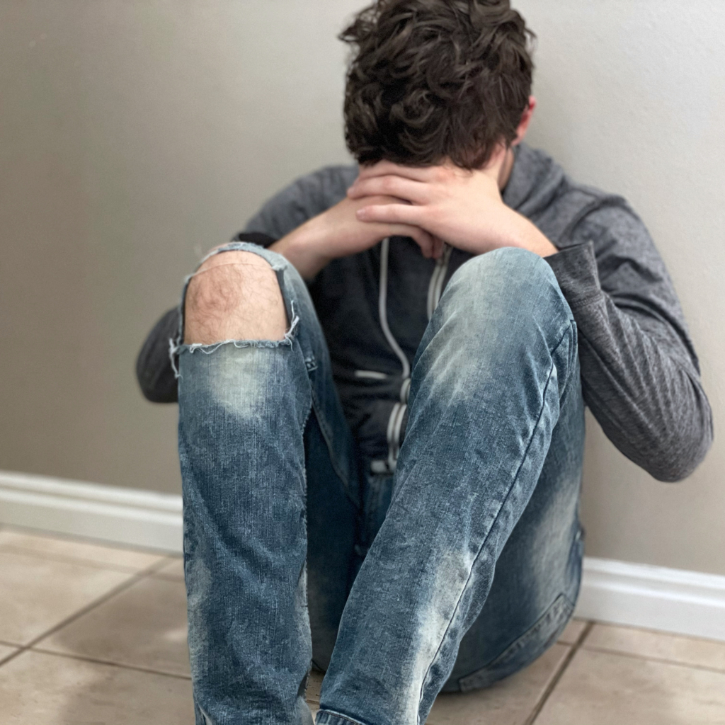 Teen sitting on the floor with head down, showing how emotional dysregulation can feel overwhelming.