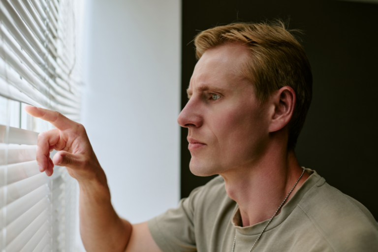 Veteran looking through window blinds at home, reflecting the guarded feeling that can follow military reintegration after deployment.