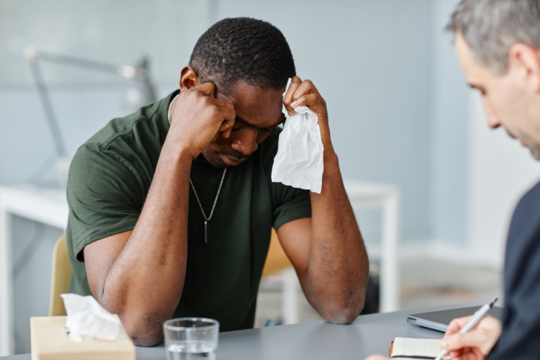 Veteran appearing distressed during a therapy session while speaking with a mental health professional about difficult experiences after military service.