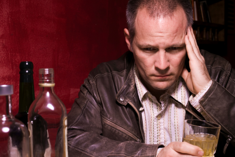 Man sitting alone with alcohol, looking stressed and withdrawn, reflecting drinking as a way to cope after difficult experiences.