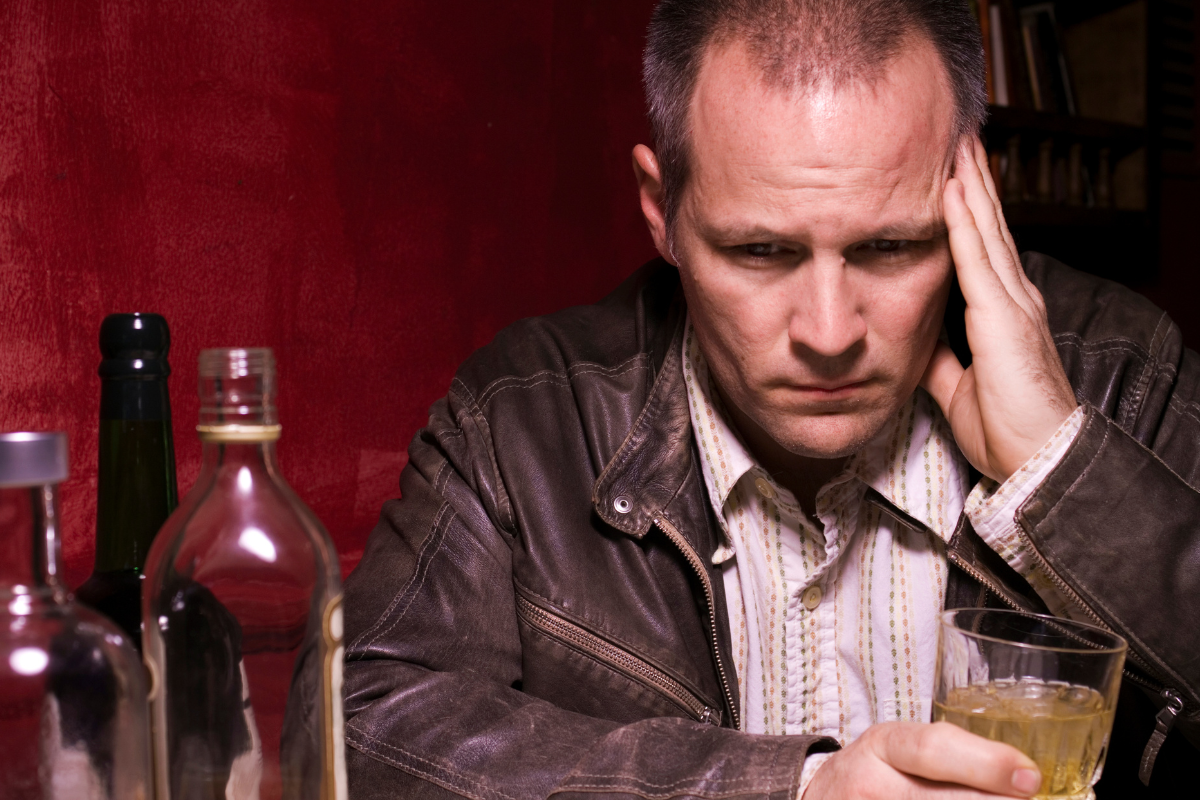 Man sitting alone with alcohol, looking stressed and withdrawn, reflecting drinking as a way to cope after difficult experiences.