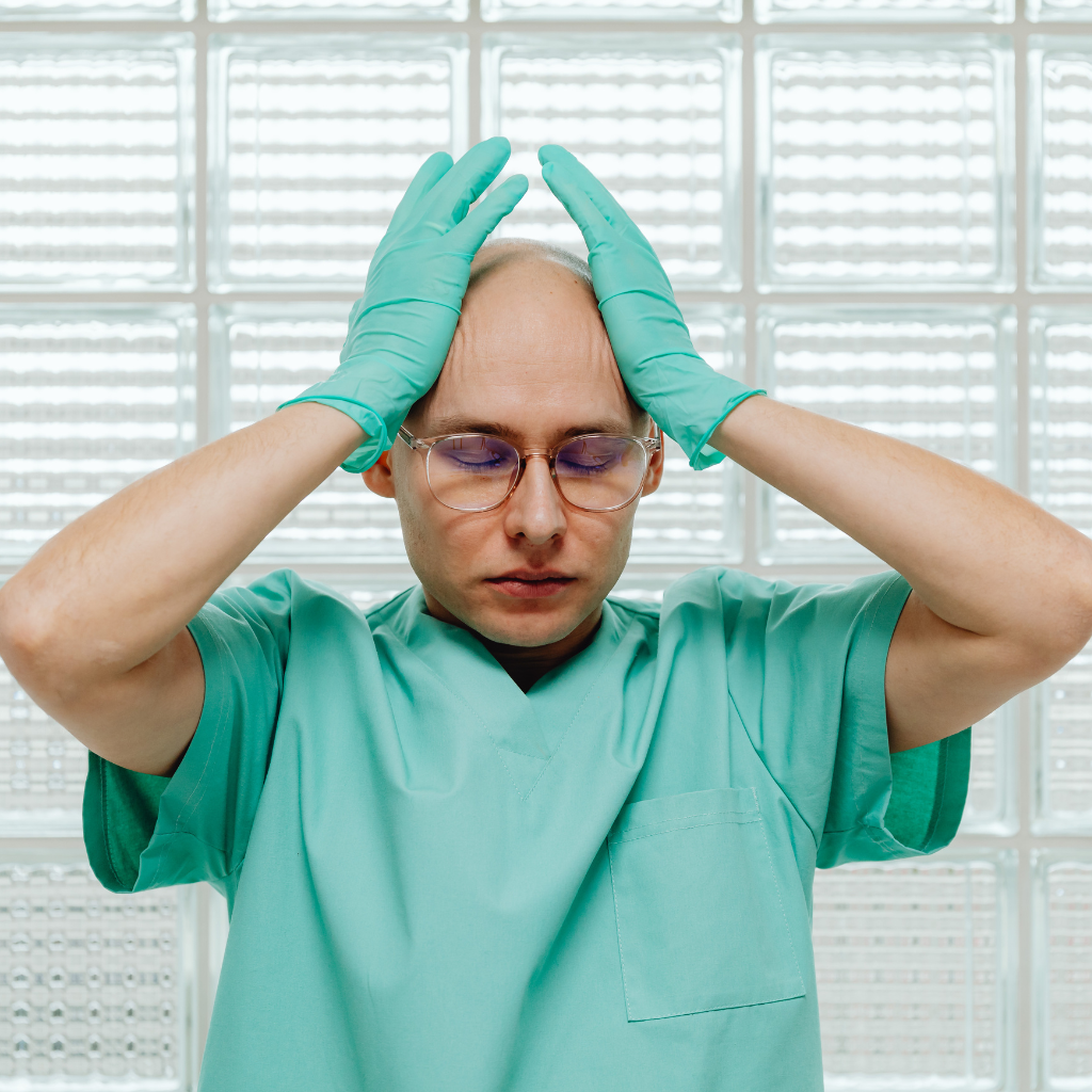 Healthcare worker in scrubs holding his head, showing the emotional and physical exhaustion that can come with high-stress care work.