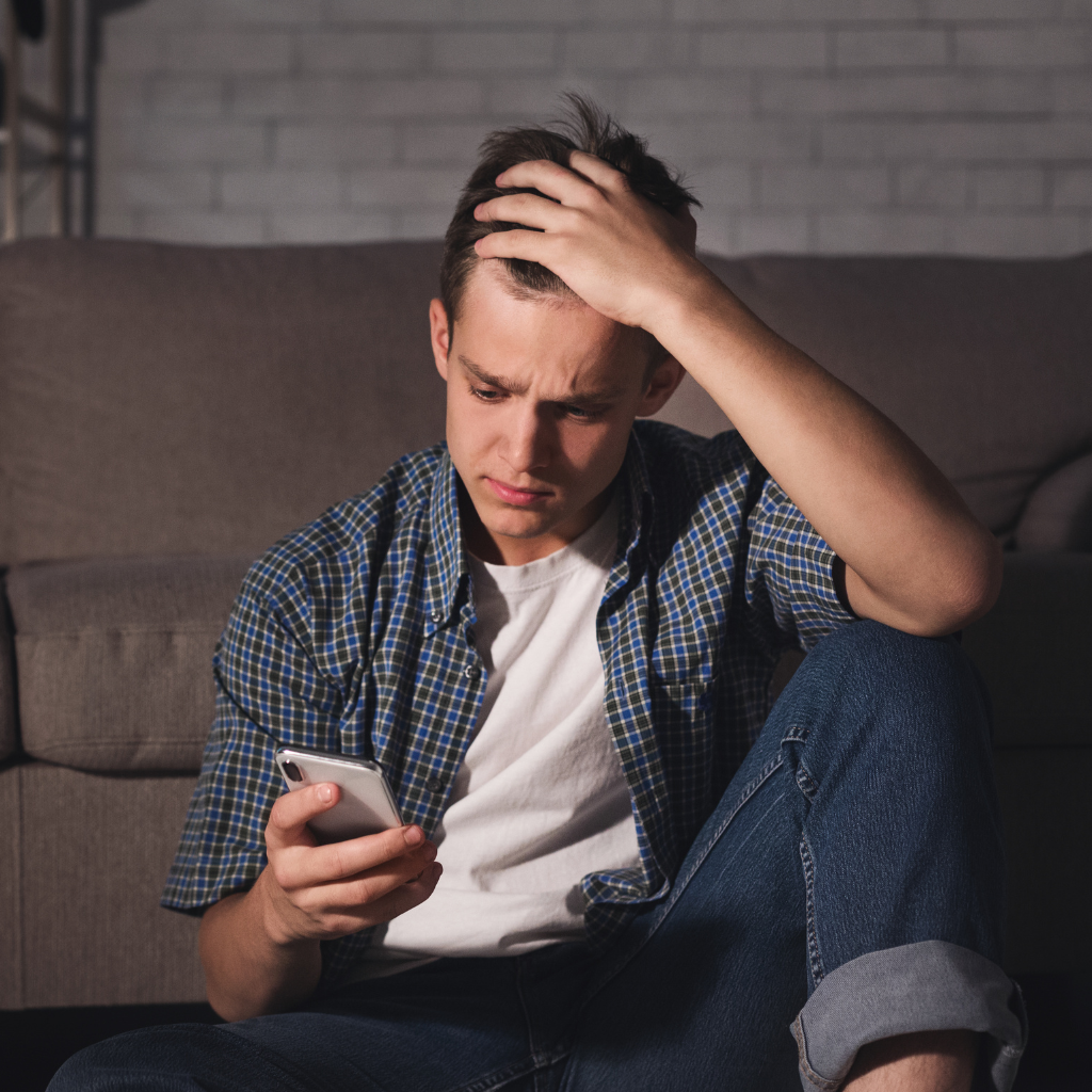 Teen looking upset while scrolling on his phone, reflecting how social comparison on social media can affect self-esteem.