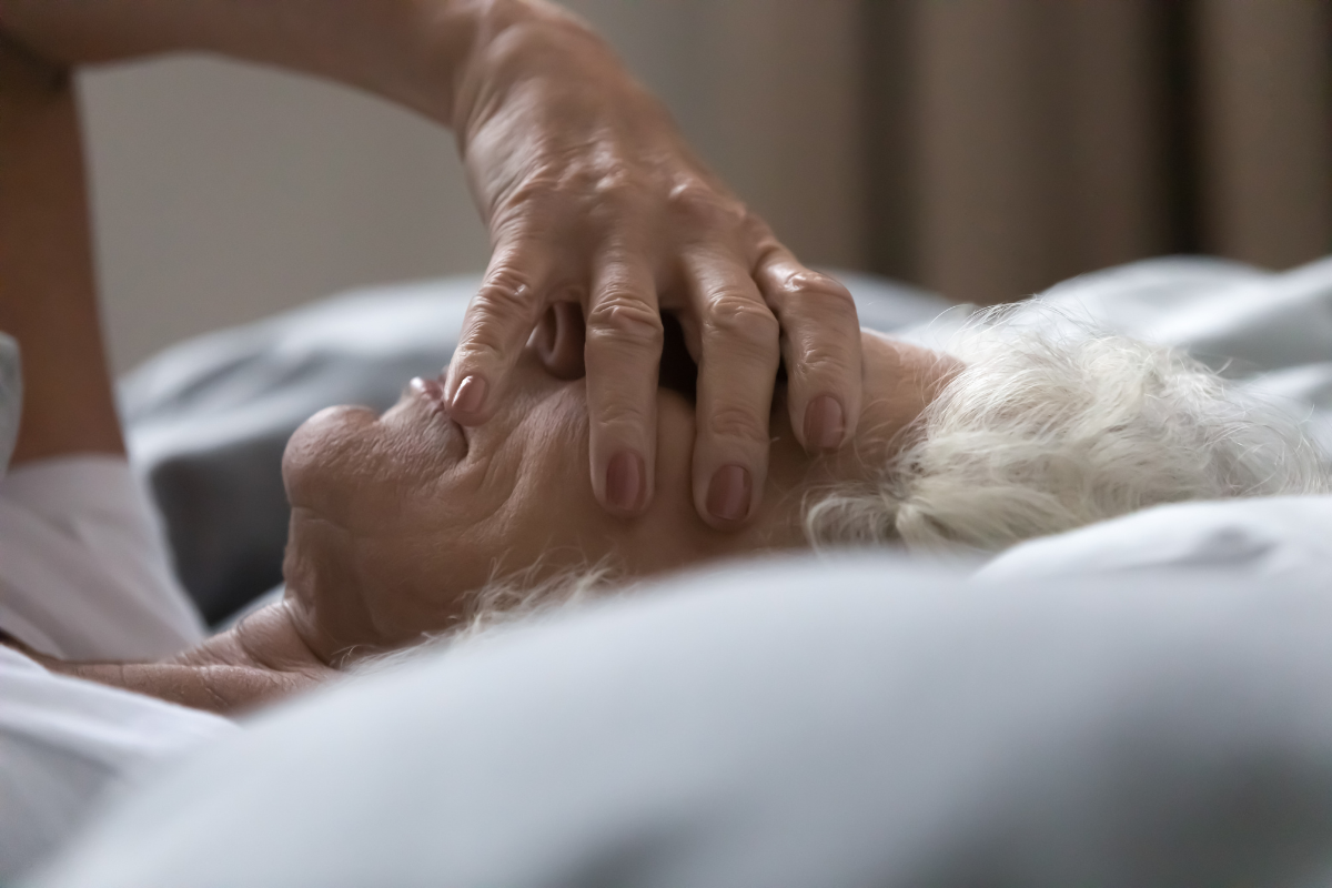 Older adult lying awake in bed with a hand over their face, showing difficulty sleeping during the night.