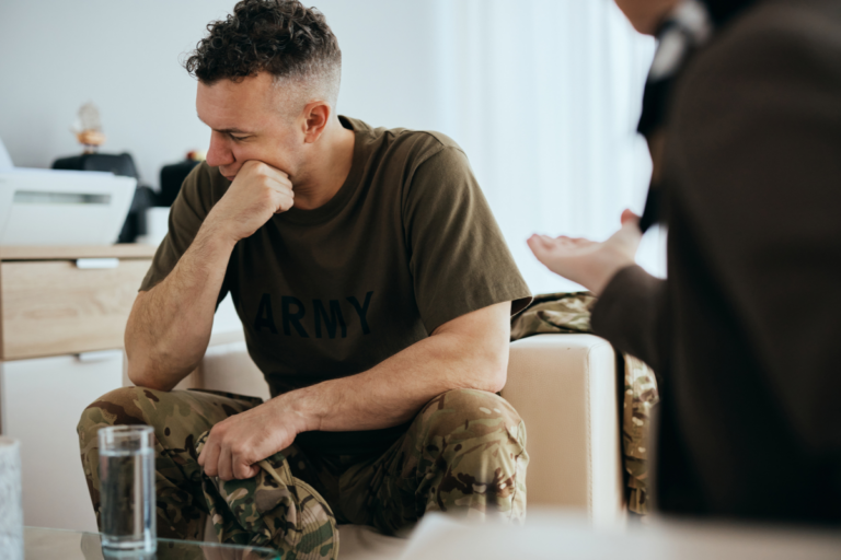 Veteran sitting with his head lowered while another person speaks with him, showing reluctance to open up about mental health concerns.