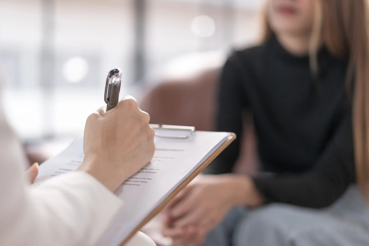 Therapist taking notes while speaking with a patient during an initial therapy consultation.