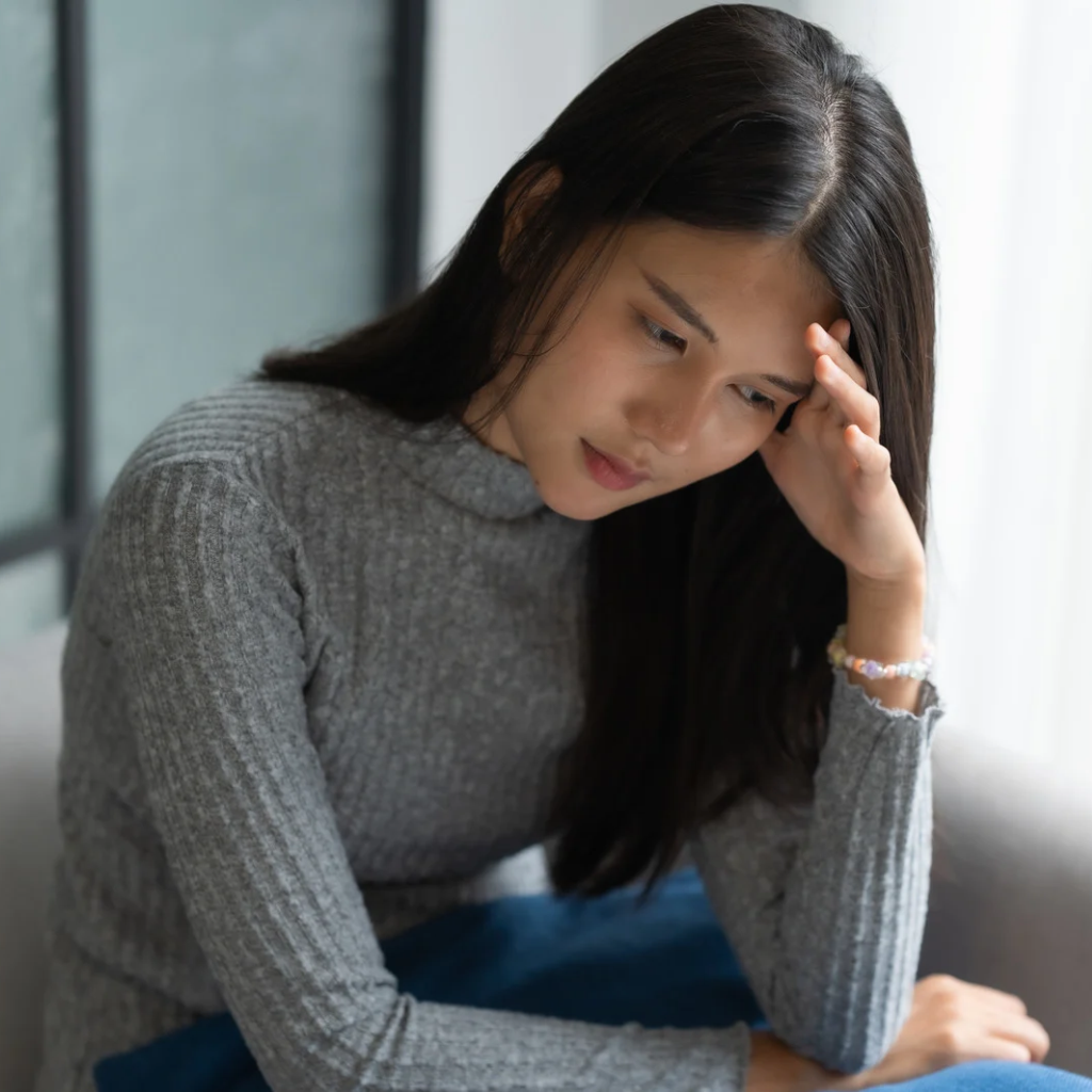 Woman sitting with her hand against her forehead, appearing emotionally overwhelmed after confronting difficult feelings.